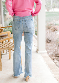 Back view of Model wearing medium washed boot cut jeans with frayed hem and high waisted fit. 