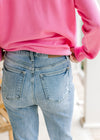 Close up of back pockets on medium washed boot cut jeans with frayed hem and high waisted fit. 
