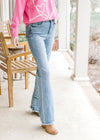 Model wearing medium washed boot cut jeans with frayed hem and high waisted fit. 