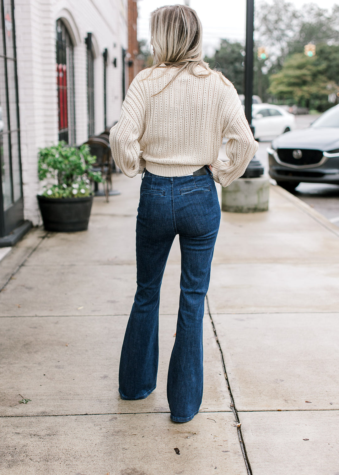 Back view of a model wearing dark, slightly flared jeans with faux back pockets. 