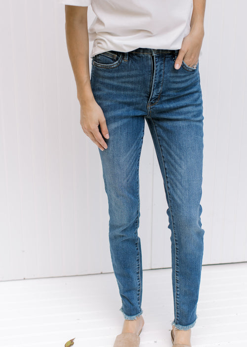 Model wearing high rise medium wash jeans with a raw hemline, tummy control and a split hem. 