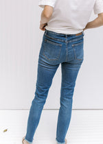 Back view of Model wearing high rise medium wash jeans with a raw hemline and a split hem. 