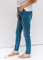 Side view of Model wearing high rise medium wash jeans with a raw hemline and tummy control. 
