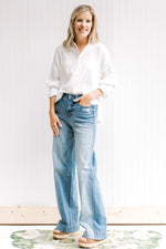Model wearing a white button up with light washed jeans that are worn at the back and front pocket. 