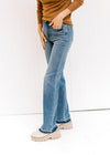 Side view of Model wearing medium wash jeans with a release hem, control top and a boot cut. 