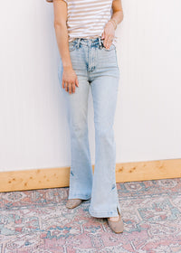 Model wearing a tee and lightwash bootcut jeans with side slits and a built in tummy control. 