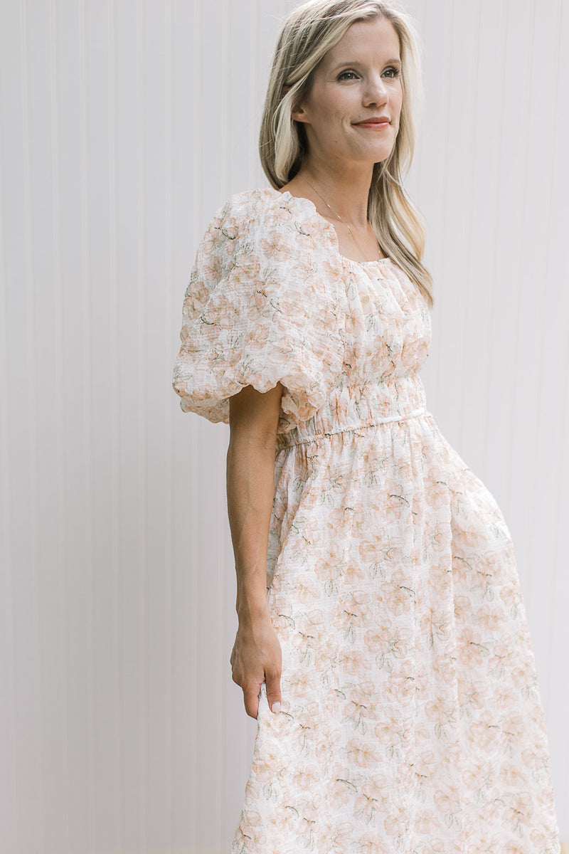 Close up of bubble short sleeves, smocked waist and a square neck o a cream top with peach flowers.