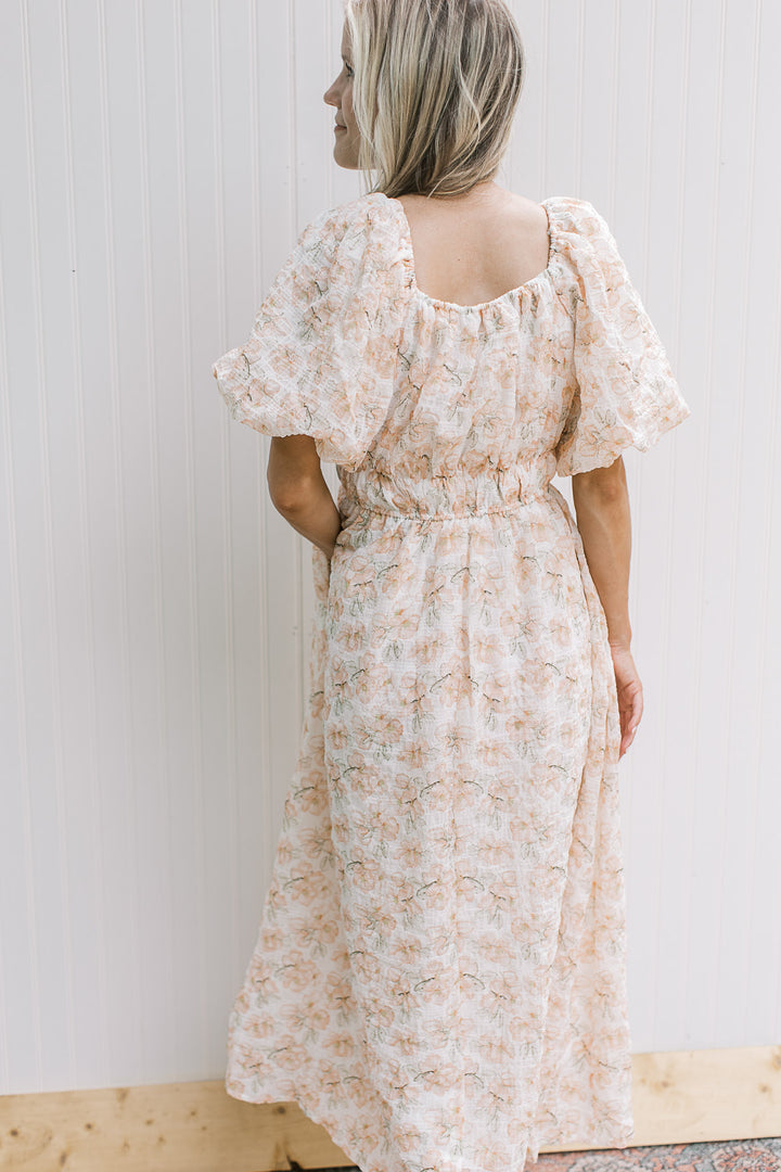Back view of Model wearing a cream dress with peach flowers, bubble short sleeves and smocked waist.
