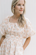 Close up of smocked waist and square neck on a cream top with peach flowers. 