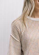 Close up of ribbed material and exposed hem on a cream and tan stripped sweater. 