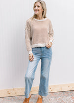 Model wearing jeans with a cream and tan striped sweater with long sleeves and extended shoulders.