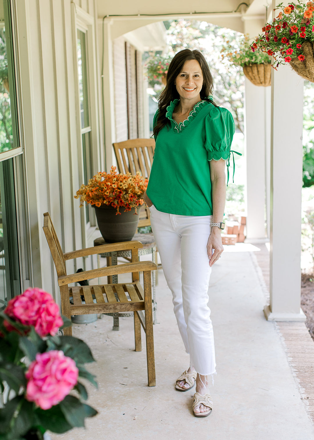 Model in white pants, sandals and a bright green top with layered scalloped neck and short sleeves.