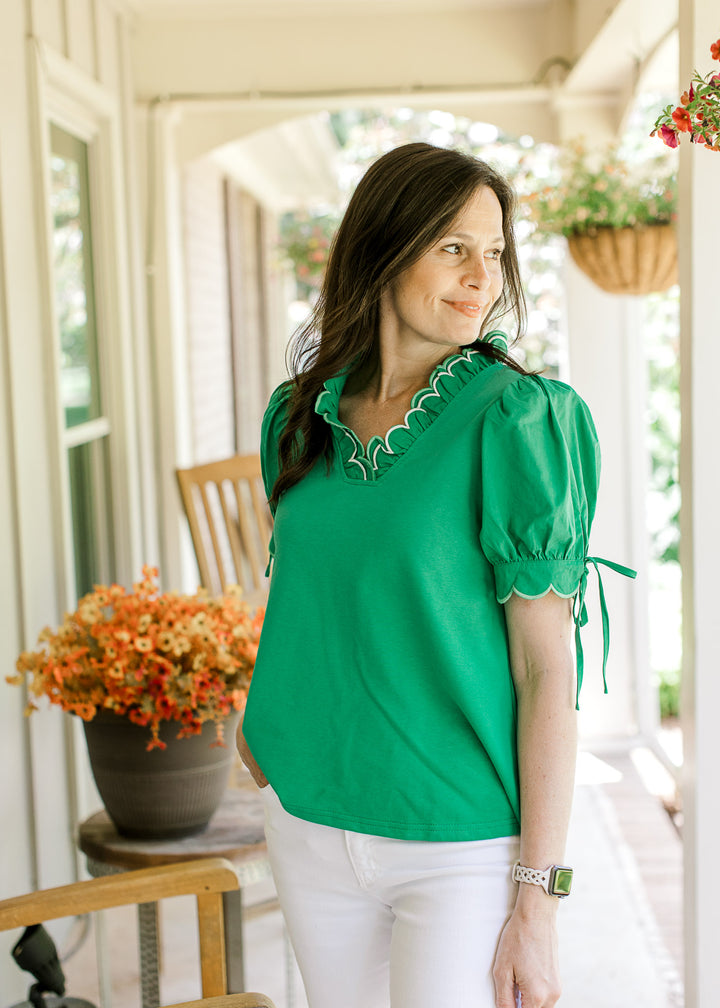 Model wearing a bright green top with layered scalloped V-neck and short sleeves with tie detail.
