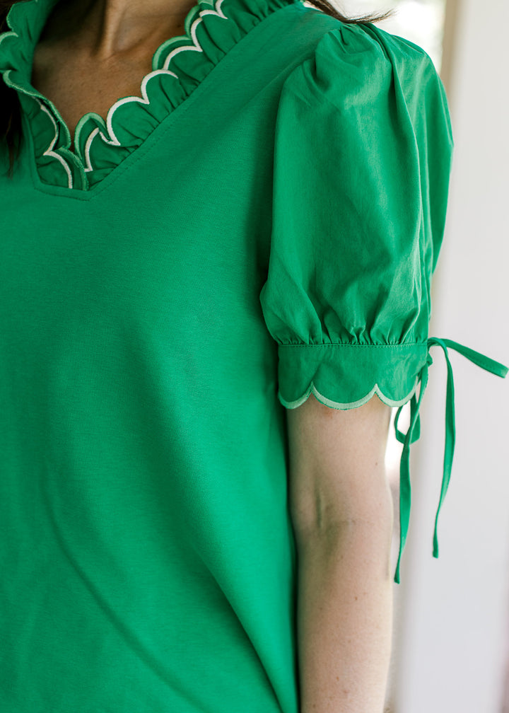 Close up of pleated short sleeves with scalloped hem and layered scalloped v-neck on green top.