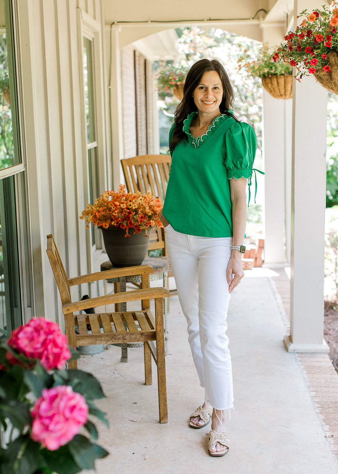 Model wearing white pants and a green top with scalloped V-neck and short sleeves with tie detail.