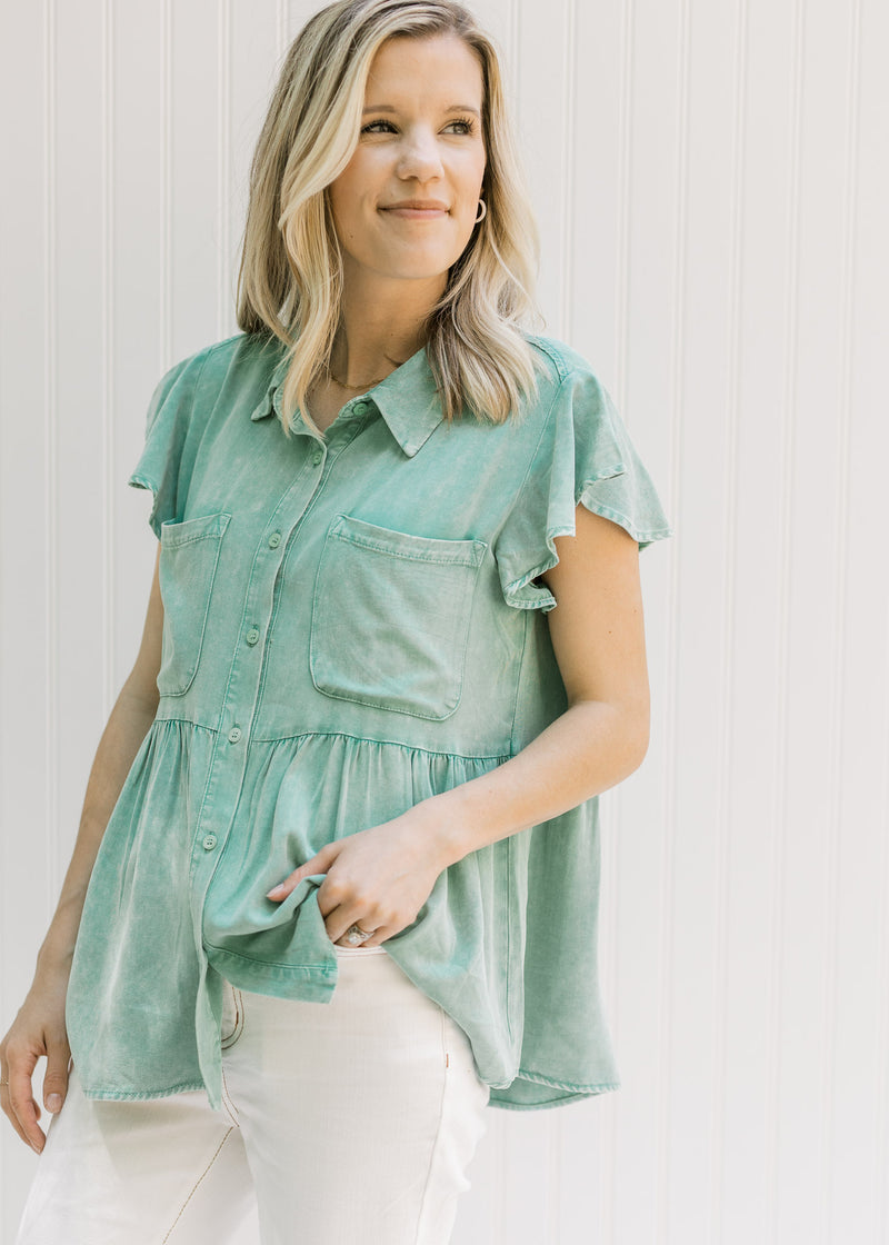 Model wearing a green chambray button up top with patch pockets and ruffle short sleeves.