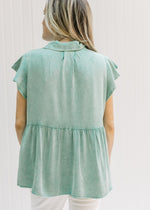 Back view of Model wearing a green button up top with patch pockets and ruffle short sleeves.
