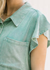 Close up view of ruffle short sleeves and patch pockets on a green chambray top. 
