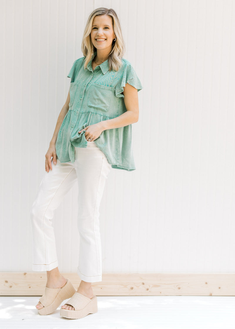 Model wearing jeans with a green chambray button up top with patch pockets and ruffle short sleeves.