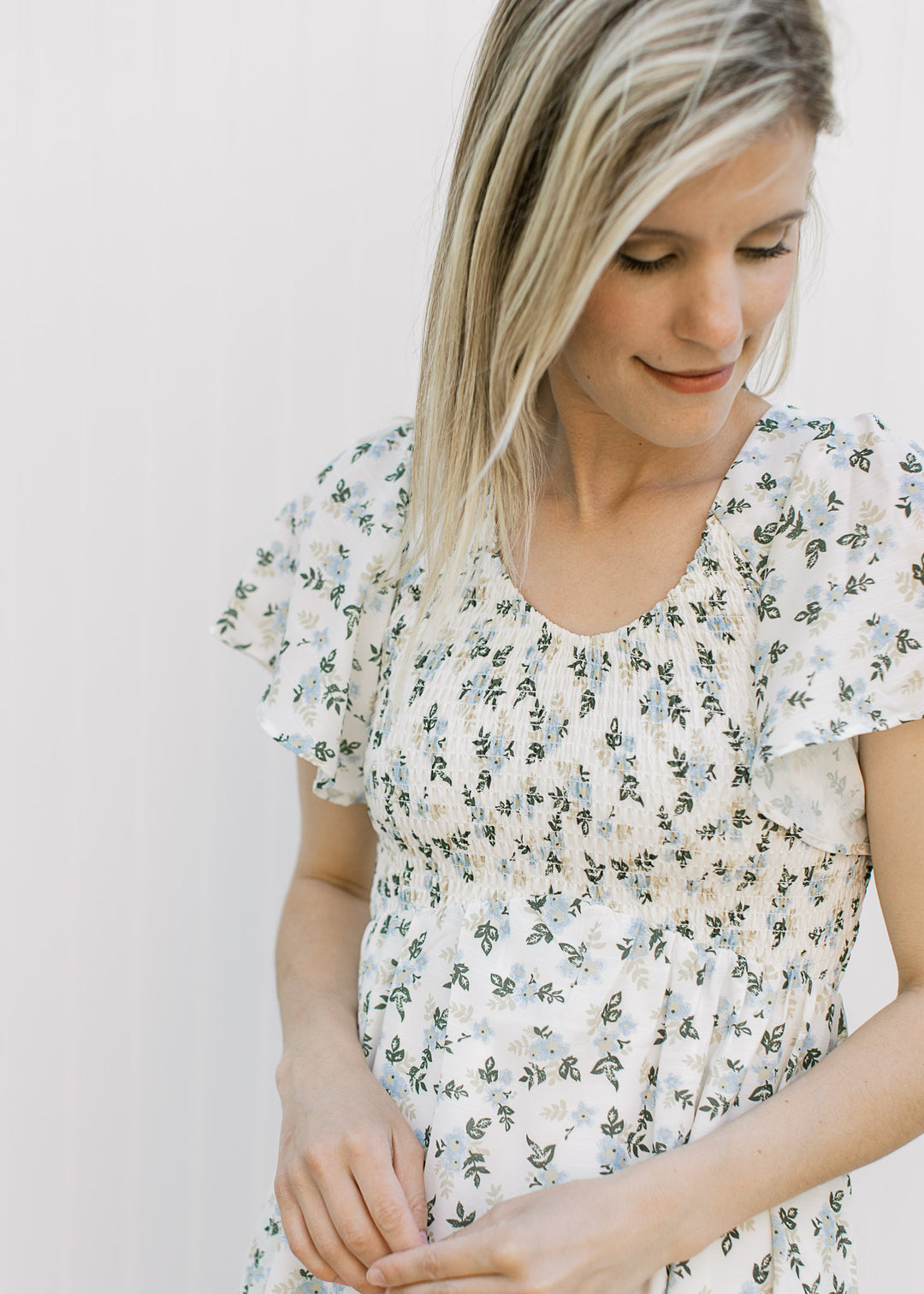 Close up of smocked bodice, v-neck and flutter short sleeves on an off white midi with floral. 