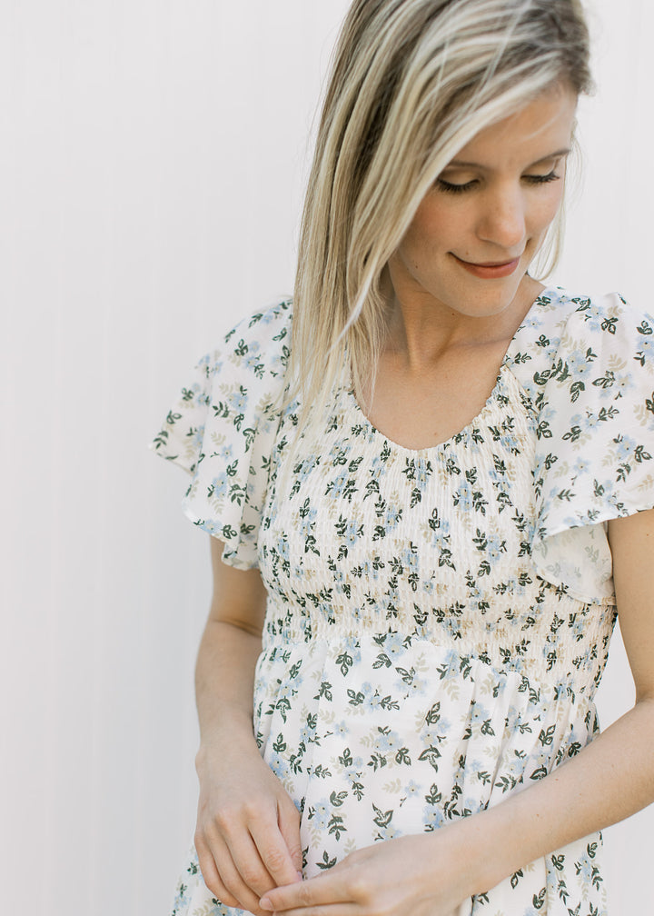 Close up of smocked bodice, v-neck and flutter short sleeves on an off white midi with floral. 