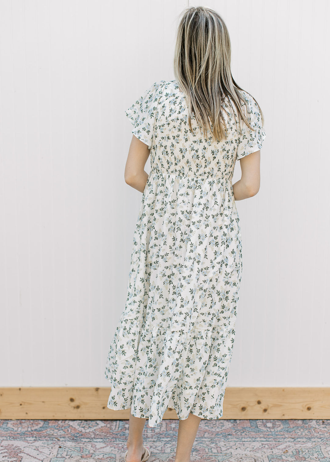 Back view of Model wearing an off white midi with floral, smocked bodice and short sleeves.