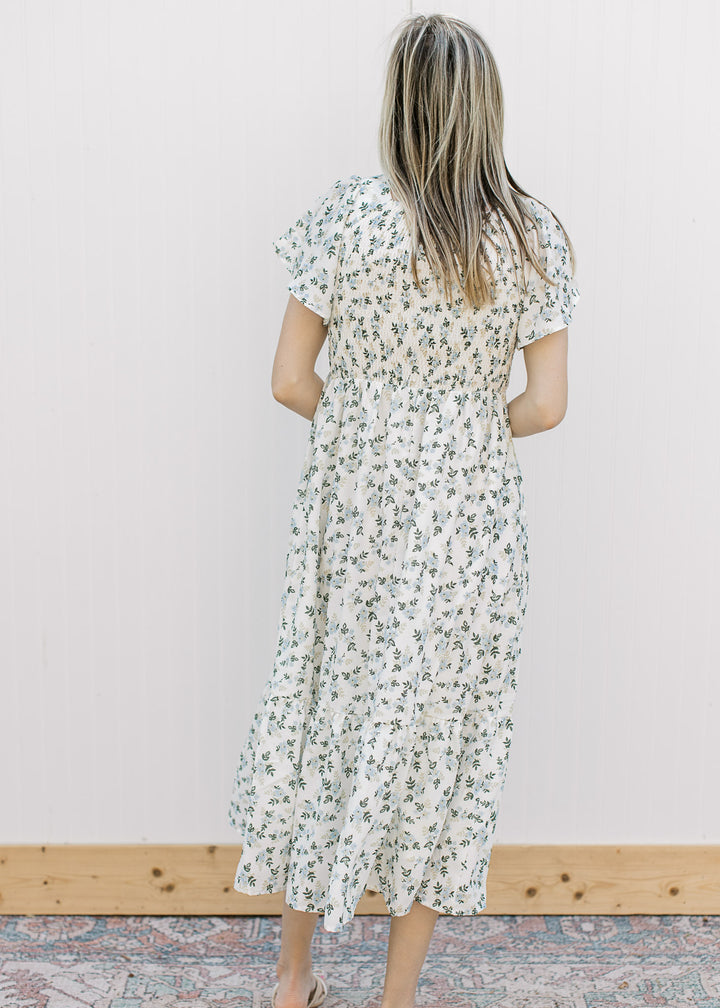 Back view of Model wearing an off white midi with floral, smocked bodice and short sleeves.