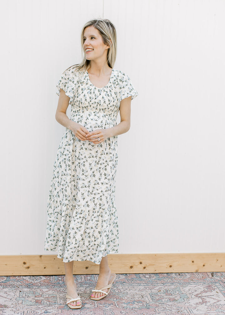 Model wearing sandals and an off white midi with blue and tan floral, v-neck and short sleeves.