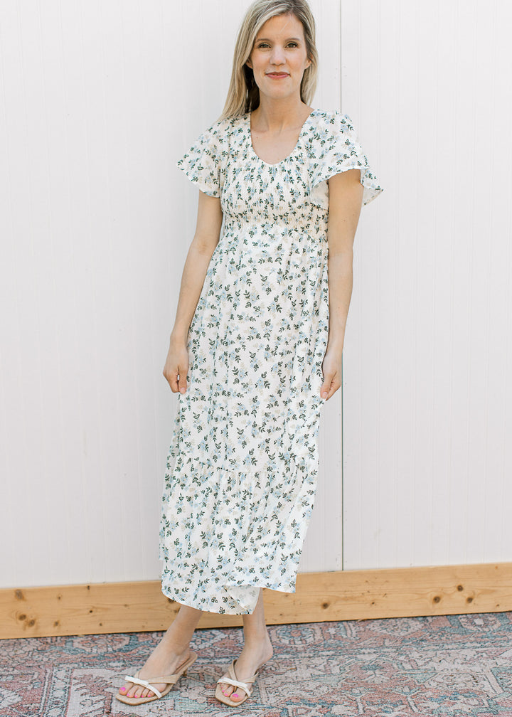 Model wearing an off white midi with blue and tan floral, smocked bodice and flutter short sleeves.