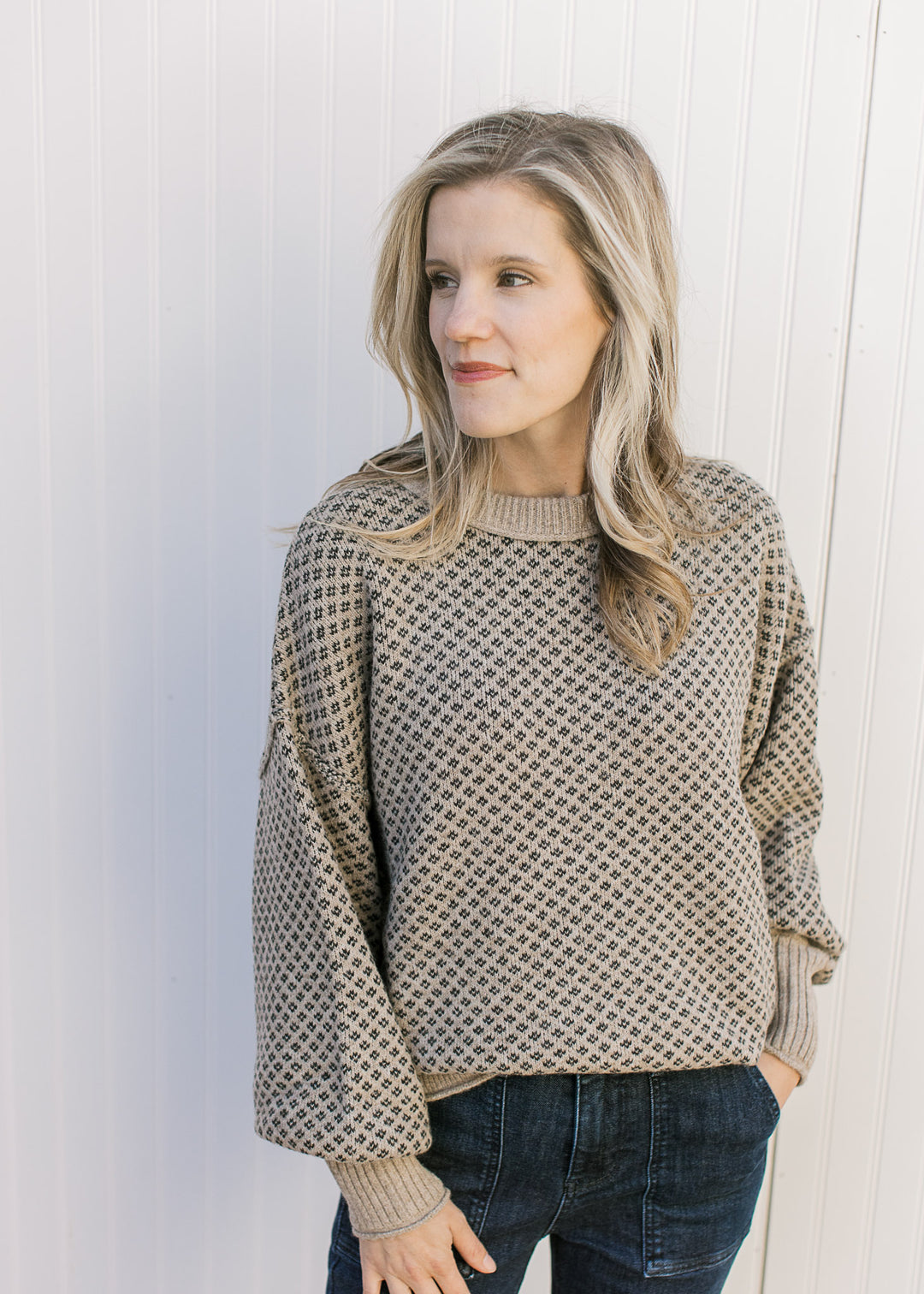 Model wearing a khaki sweater with a navy pattern, rolled hem and cuffs with exposed seam accents.