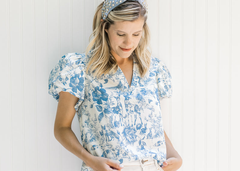 Model wearing a headband with a white top with blue floral and animal patterns and short sleeves. 