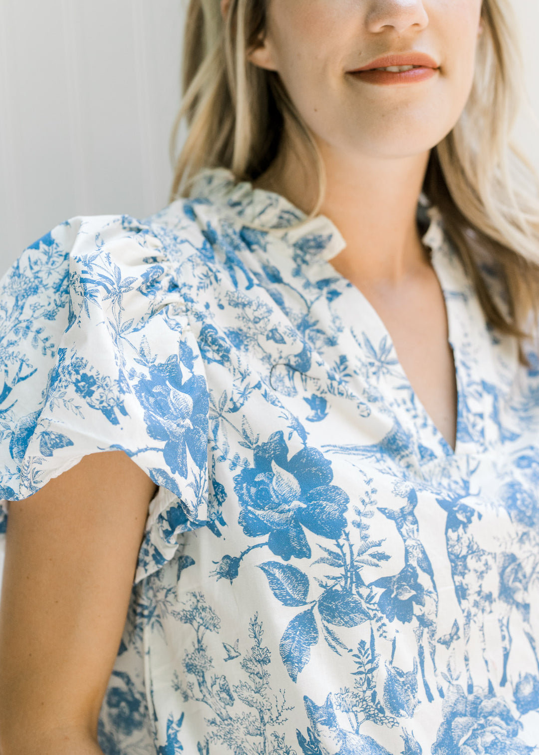 Close up view of v-neck and short puff sleeves on a white top with blue animal and floral pattern.