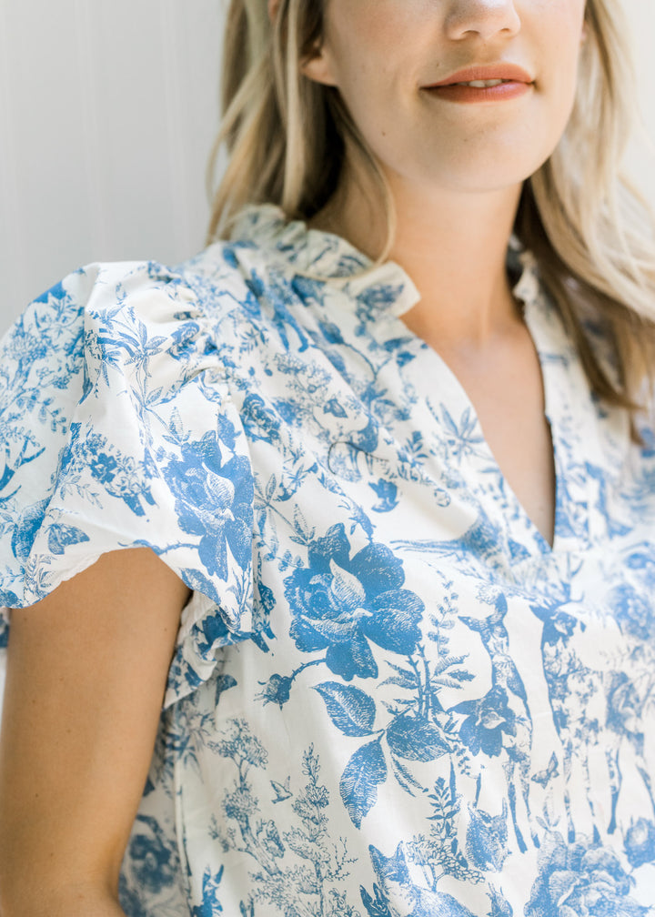 Close up view of v-neck and short puff sleeves on a white top with blue animal and floral pattern.
