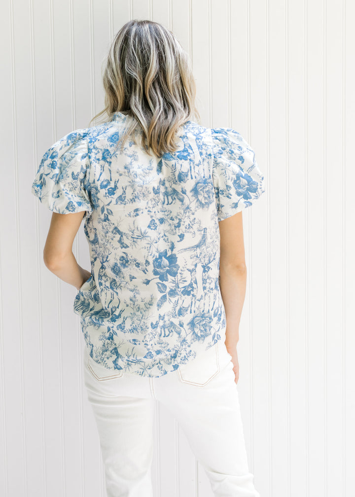 Back view of Model wearing a white v-neck top with blue floral and animal patterns and short sleeve.