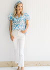 Model wearing white jeans with a white top with blue floral and animal patterns and sandals.
