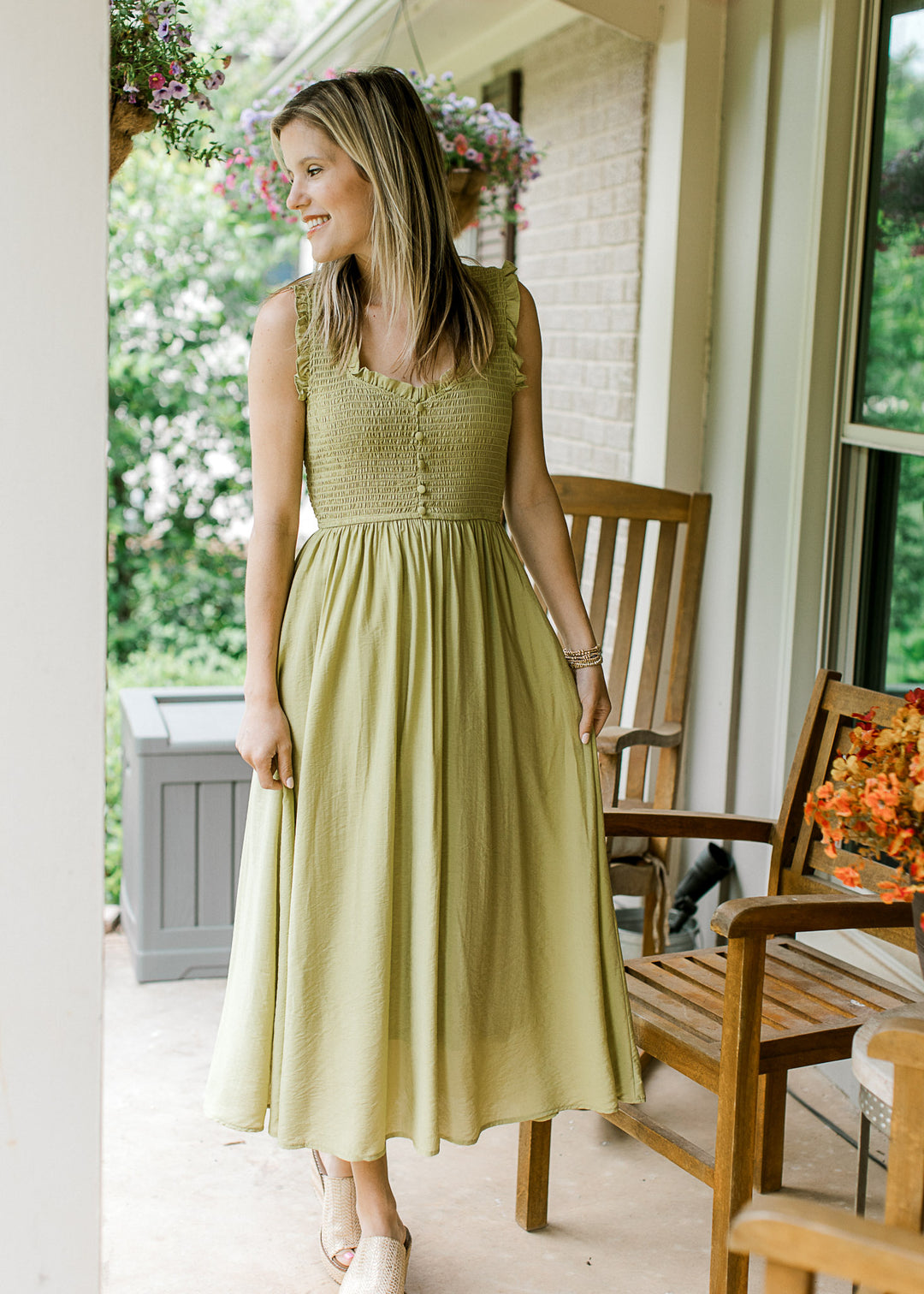Model wearing wedges and a sleeveless green midi with a smocked bodice with a v-neck with ruffle.