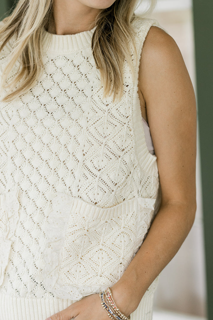Close up of patch pockets lined with lace on a model in a cream knit sleeveless sweater. 