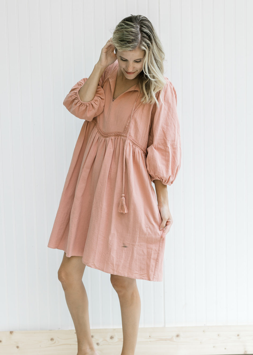 Model wearing a clay dress with embroidered detail, v-neck with tie and 3/4 bubble sleeves. 