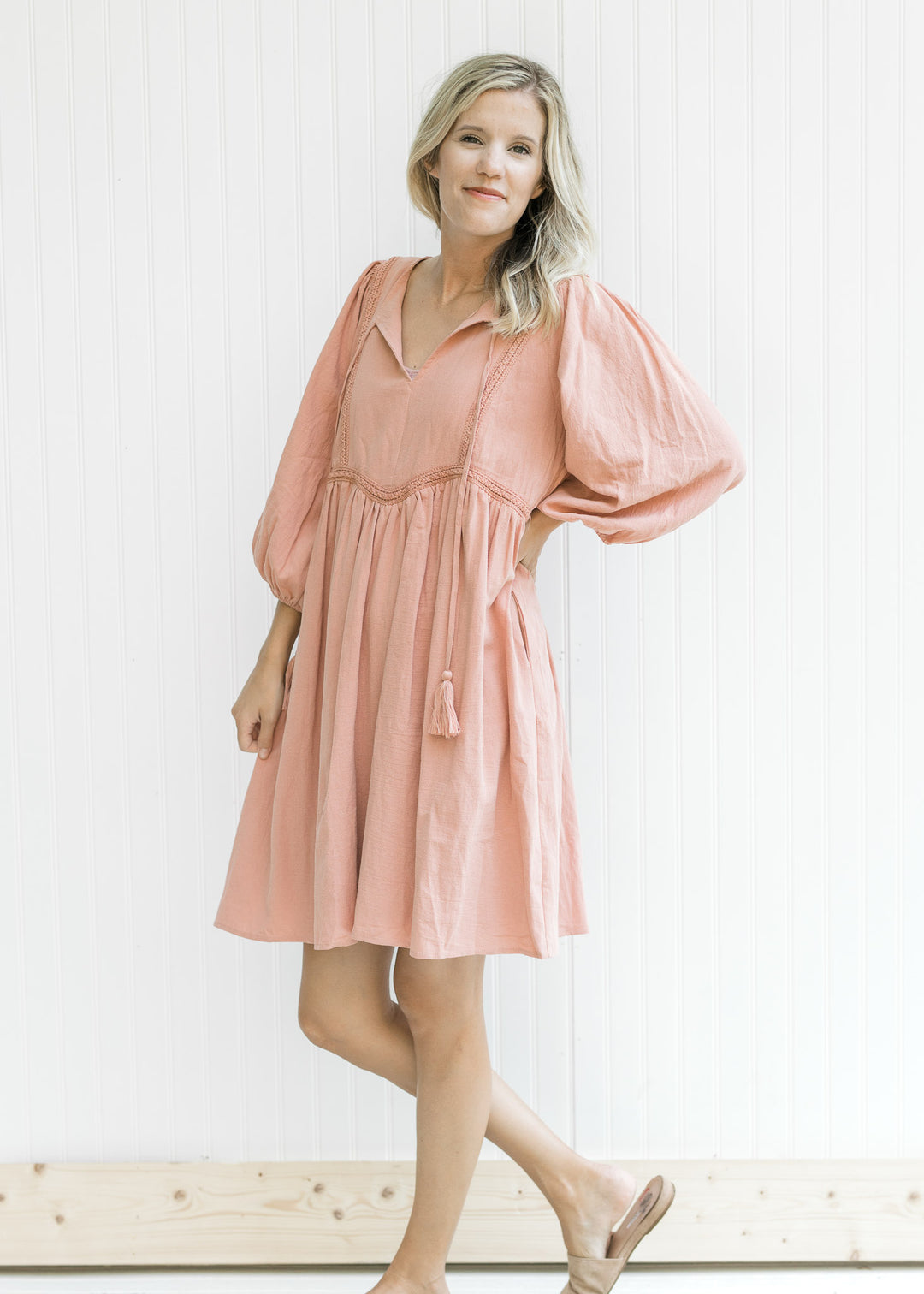Model wearing sandals with a clay colored above the knee dress with an embroidered detail. 