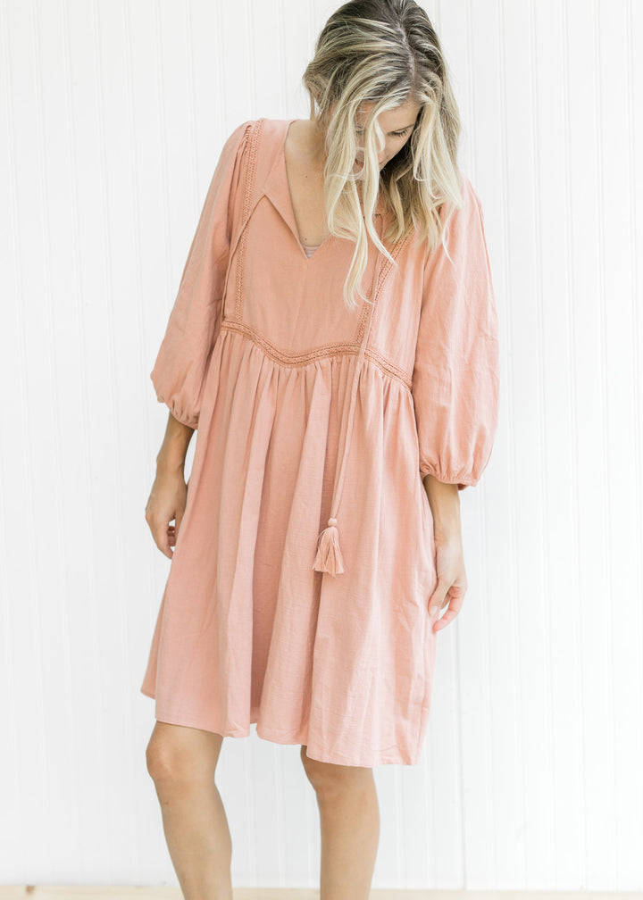 Model wearing a clay colored dress with embroidered detail, v-neck with tie and 3/4 bubble sleeves. 
