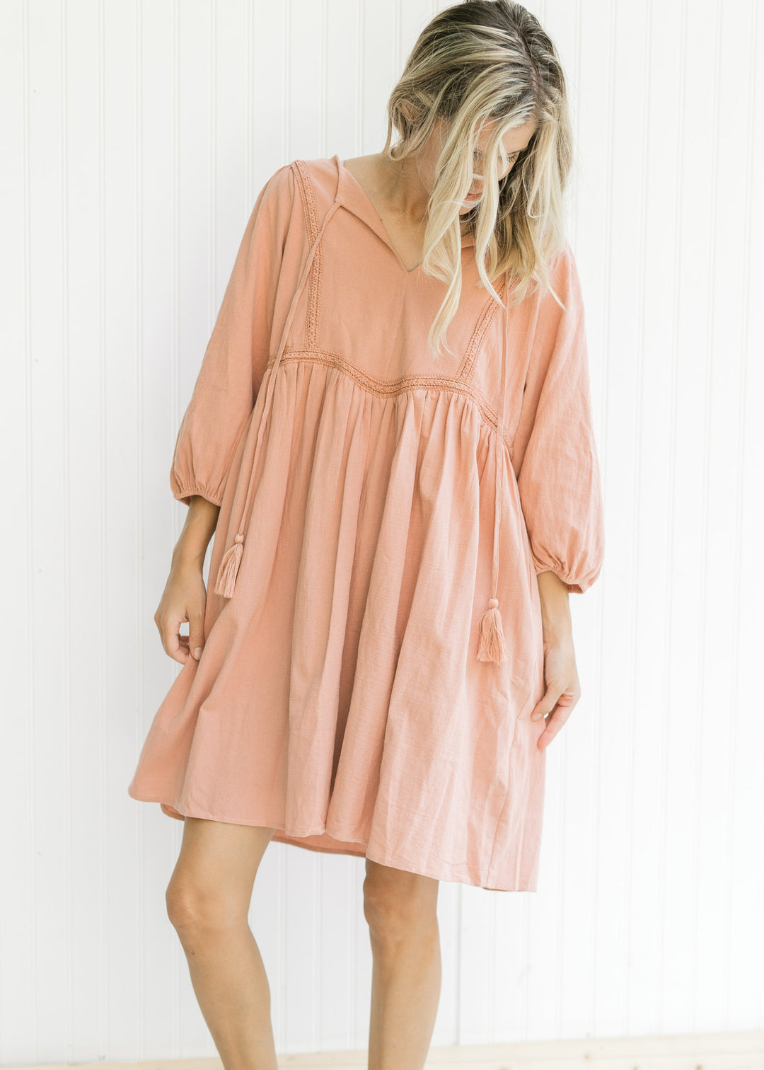 Model wearing a clay fully lined dress with embroidered detail, v-neck with tie and bubble sleeves. 