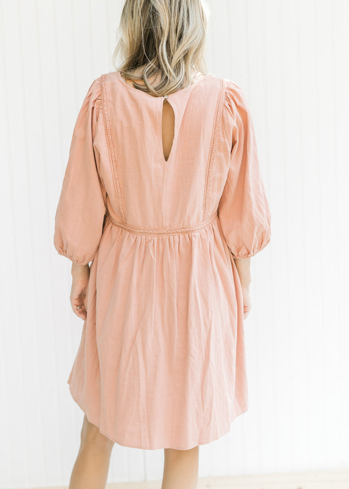 Back view of Model wearing a clay dress with embroidered detail, v-neck with tie and bubble sleeves.