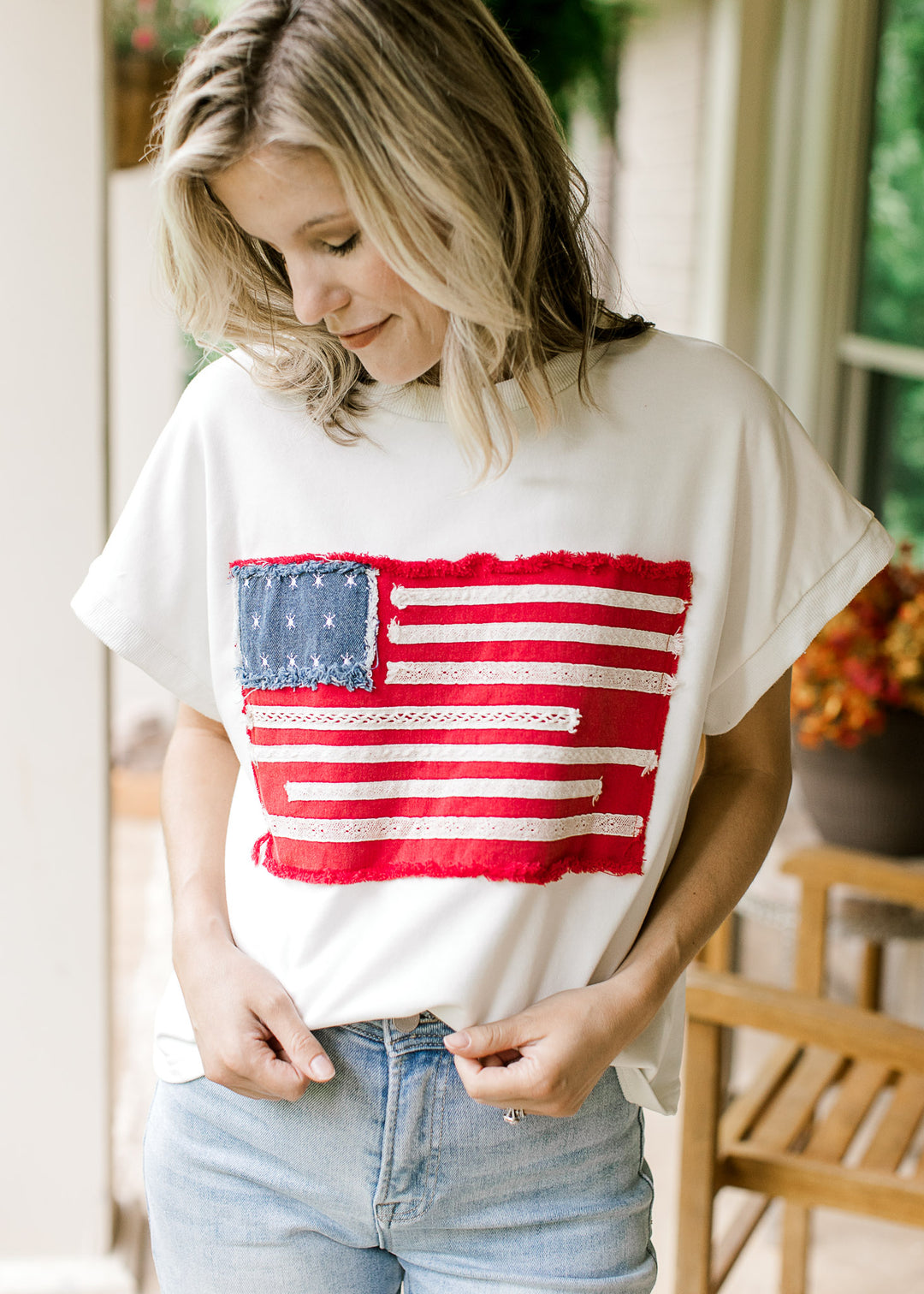 Model wearing an off-white top with American flag graphic, round neck and  cap sleeves.