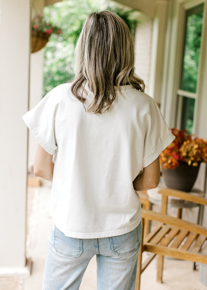 Back view of Model wearing an off-white top with American flag graphic, round neck and cap sleeves.