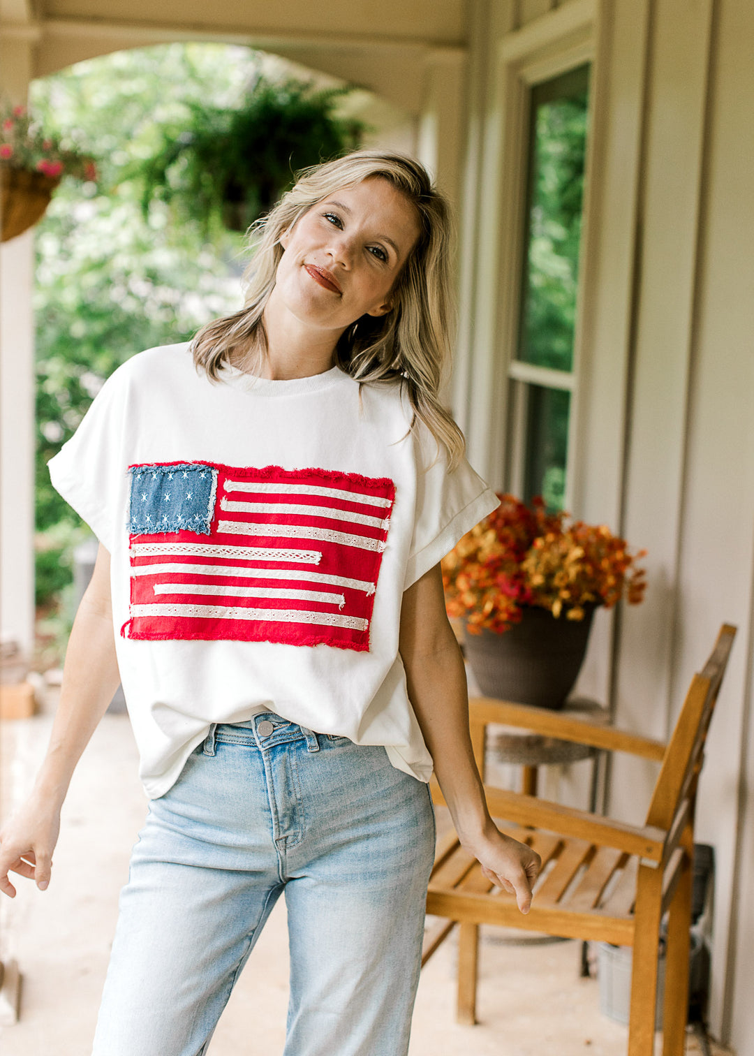 Model wearing an off-white tee with American flag graphic, round neck and  cap sleeves.