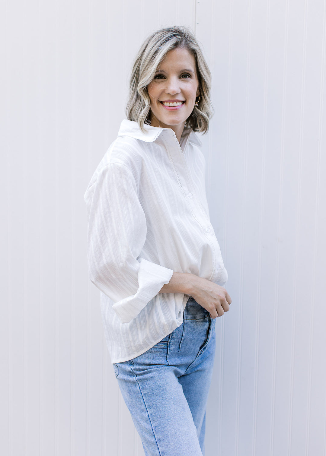 Model wearing a white, button up top with lace trim at placket and flap collar and long sleeves. 