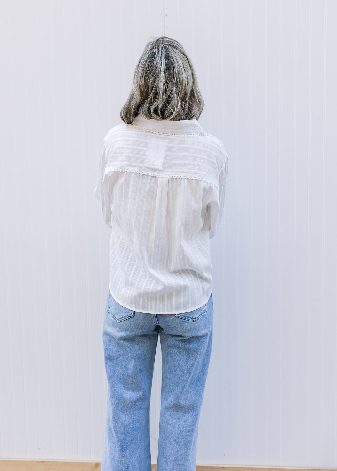 Back view of model wearing a white top with flap collar, long sleeves and subtle stripe detail.