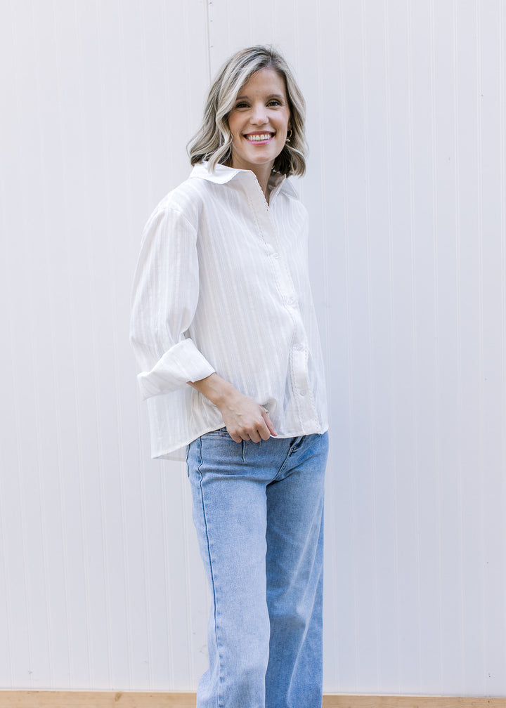 Model wearing jeans and a white, button up top with lace detail and flap collar and long sleeves. 