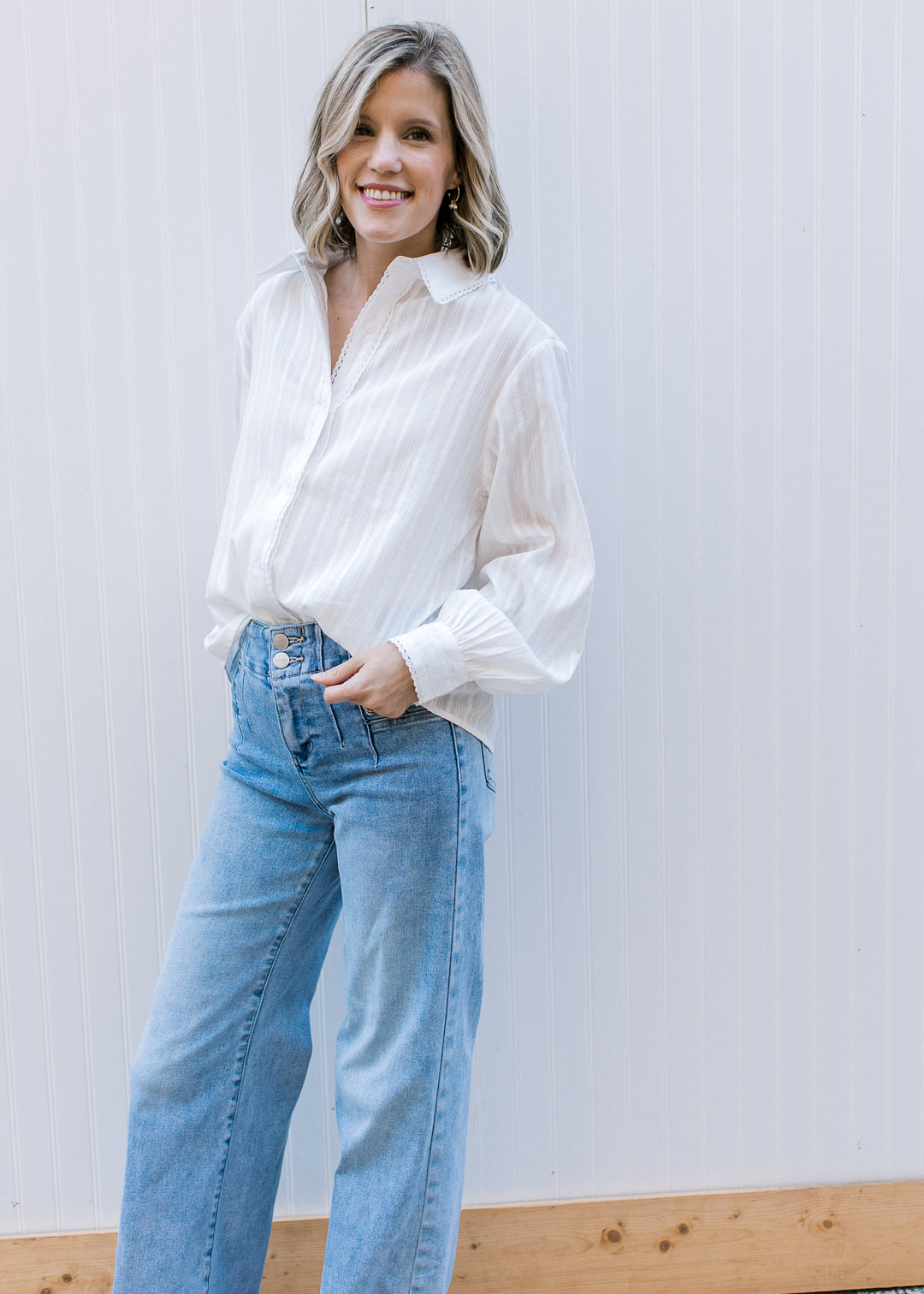 Model wearing a white, button up top with lace trim detail, flap collar and long sleeves with cuff. 