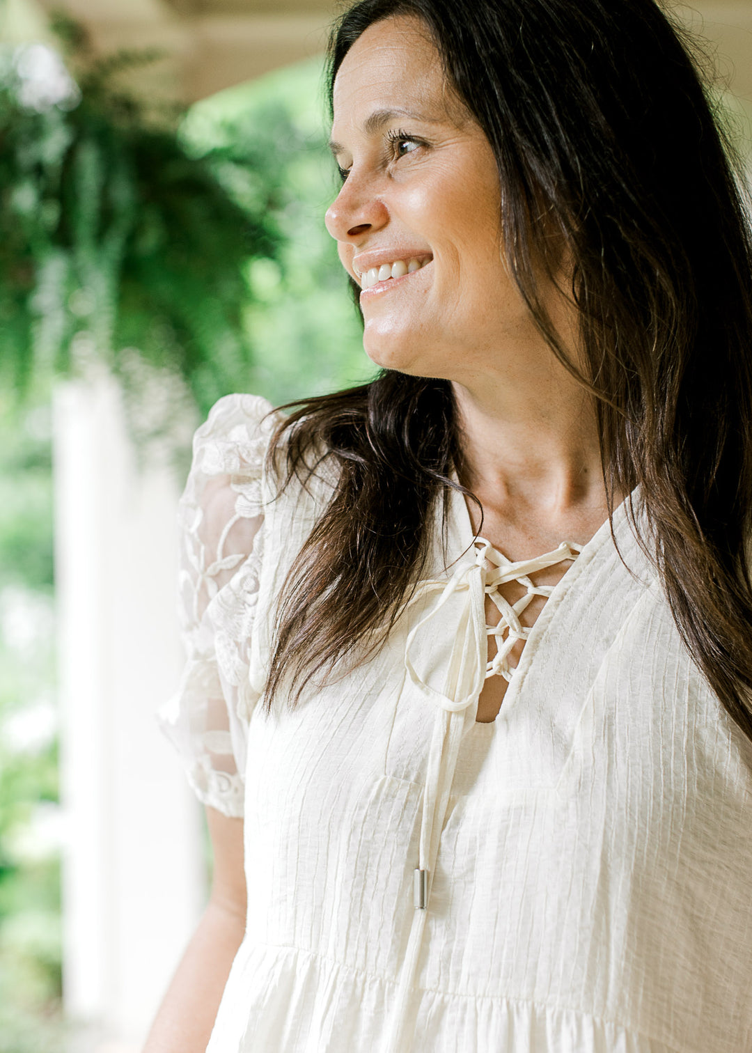 Close up of lace up v-neckline and floral sheer bubble short sleeves on a cream top.  